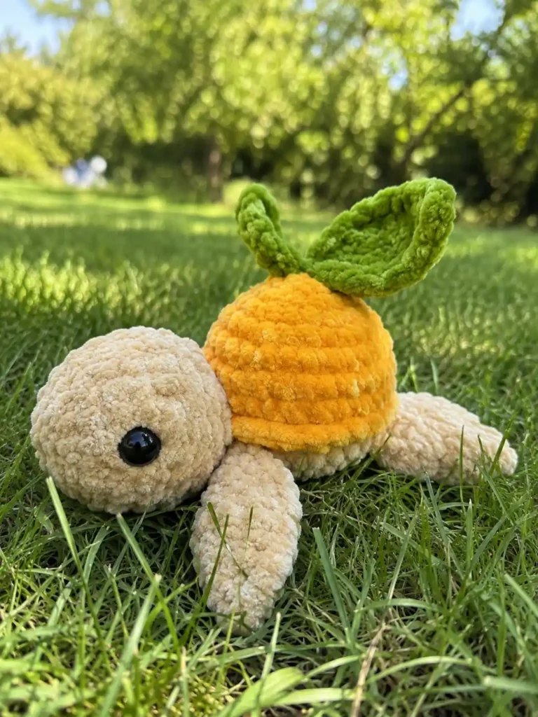 An orange and tan plush toy with green leaves sitting on green grass for the mini turtle crochet pattern free.