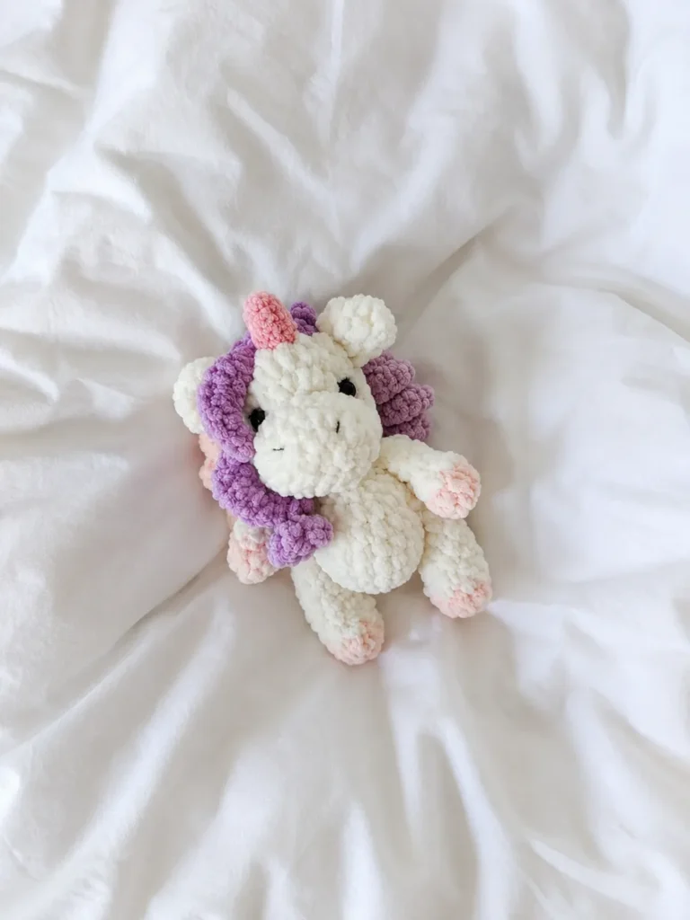 White velvet yarn toy from our mini unicorn crochet pattern free, resting on soft white wrinkled bedding.