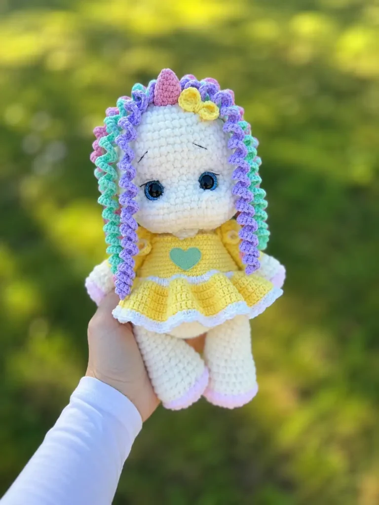 Hand holding a white chenille unicorn outdoors against a green background. Try this crochet unicorn amigurumi pattern free.