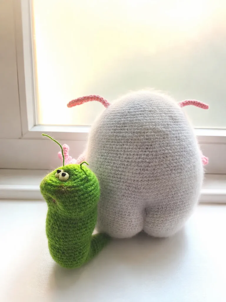 Back of fluffy monster by a green yarn caterpillar on a windowsill for the pukhlya and zhuzhik amigurumi pattern free.