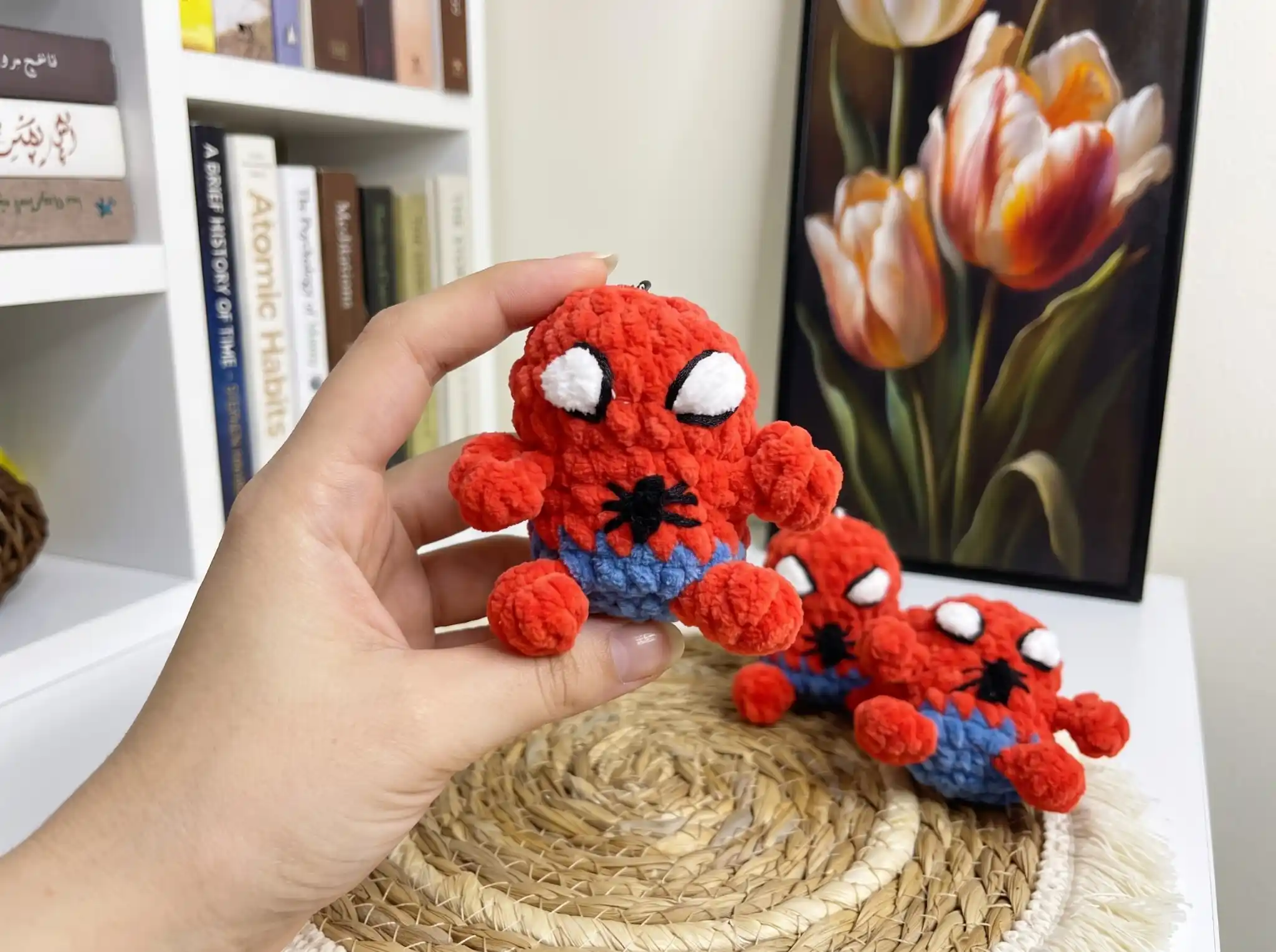 A small red and blue crocheted Spider-Man amigurumi keychain with an embroidered emblem, held in a hand.