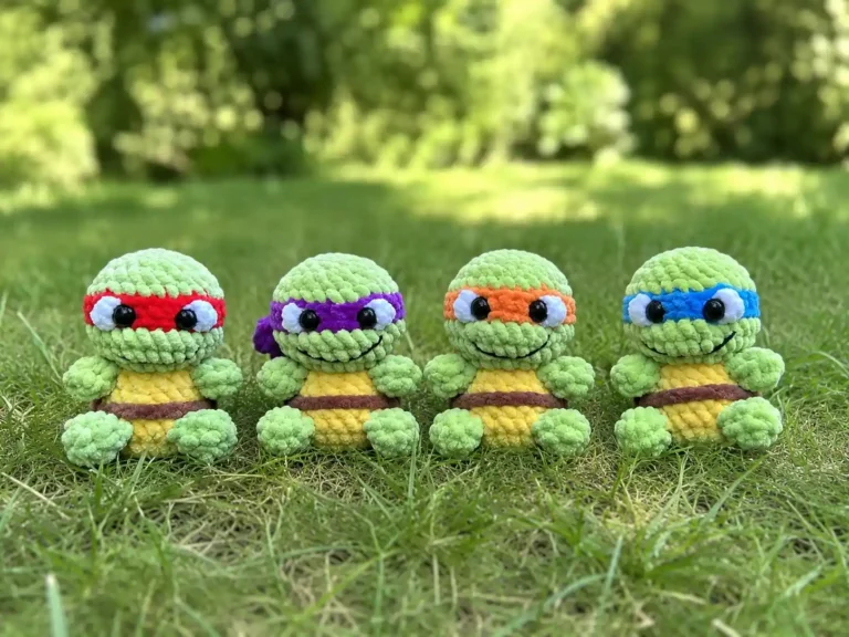 Four mini crochet teenage mutant ninja turtles amigurumi dolls with colored masks sitting together in grass.