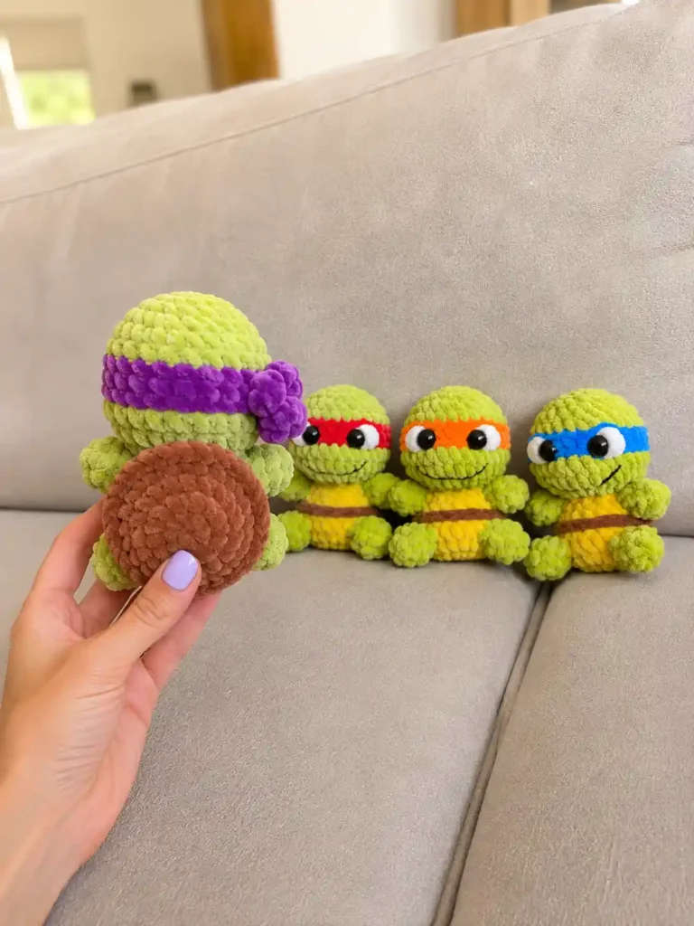 Hand holding the brown shell of a chunky yarn toy from a teenage mutant ninja turtles amigurumi free pattern on a couch.