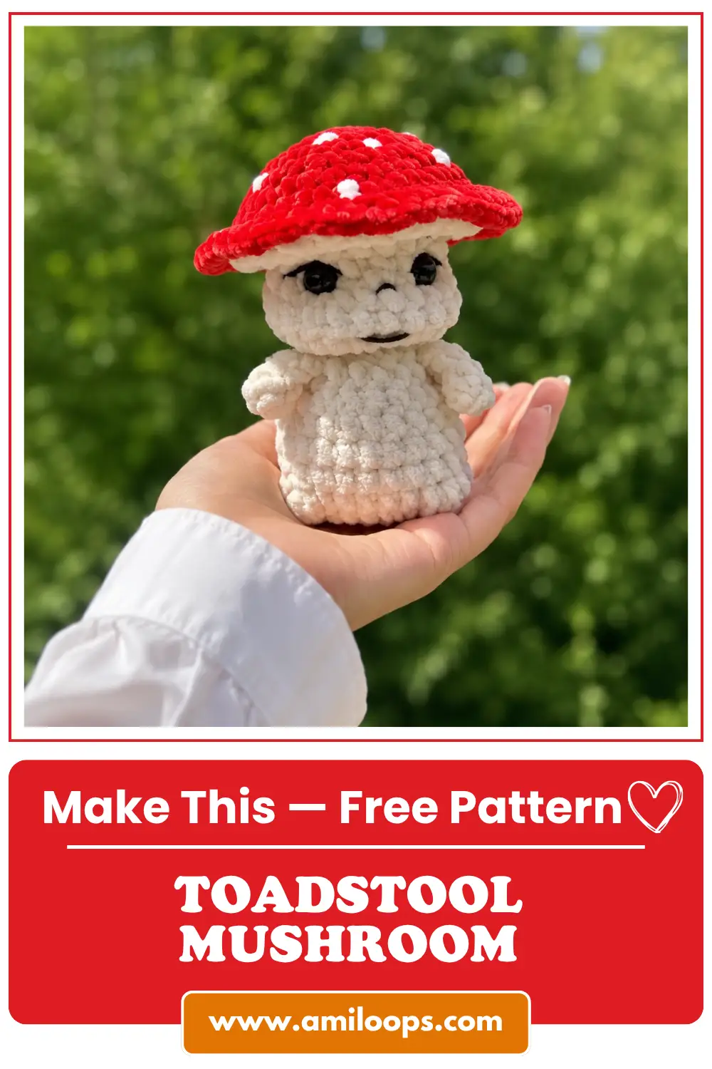 Hand holding a red and white toadstool mushroom amigurumi pattern in chunky yarn against green foliage.