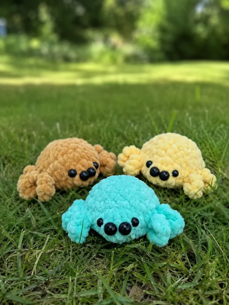 Three plush toys in brown, yellow, and mint sitting on green grass, made from a crochet spider amigurumi free pattern.