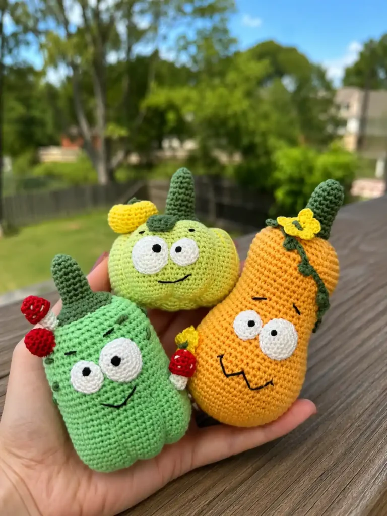 A hand holds three colorful yarn gourds from the silly pumpkin amigurumi pattern showcasing mint, green, and orange designs.