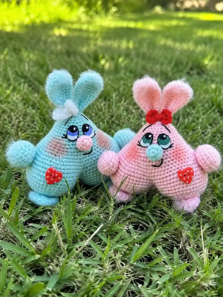 A blue and pink crochet pair sitting on sunny grass, showing the valentine heart bunnies amigurumi pattern free.