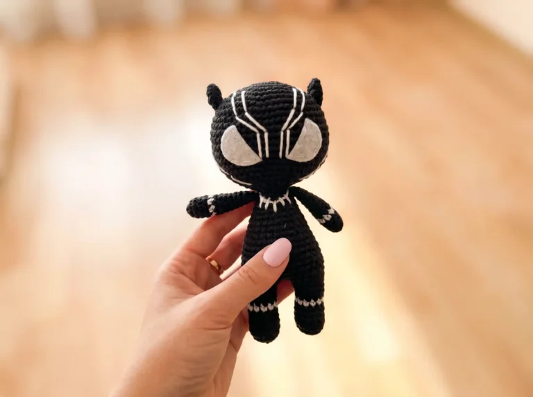 A crochet panther amigurumi held in a hand, showing its black yarn body and white felt eyes.