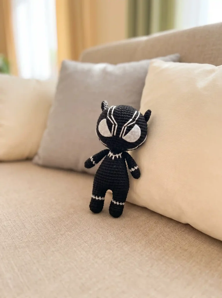 Dark yarn black panther amigurumi standing against a cream pillow on a beige fabric sofa.