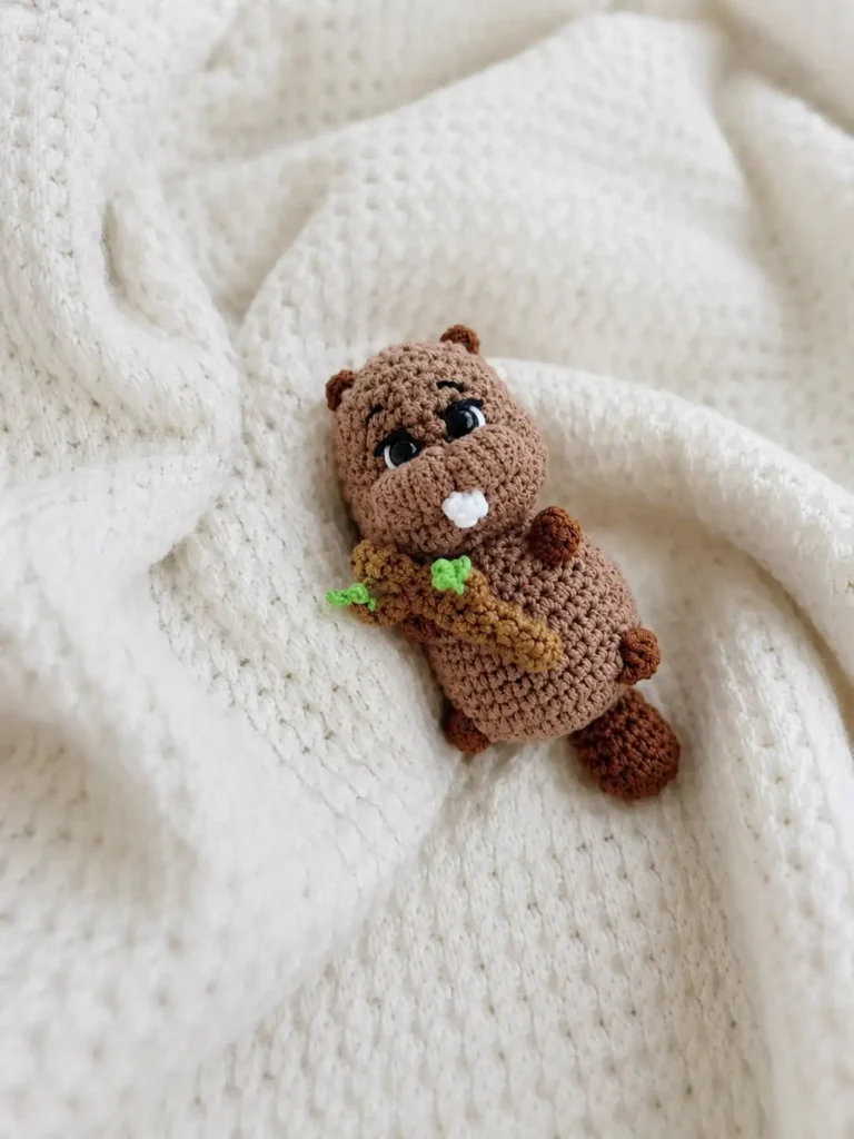 Small yarn beaver with a wooden branch on a cream knit blanket made with the Bobyor crochet pattern.