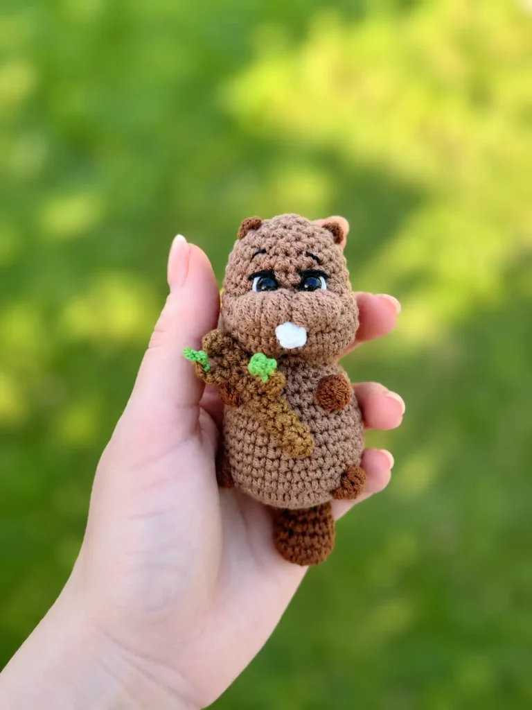 Hand holding a cute brown amigurumi beaver outside on green grass from the Bobyor crochet pattern.