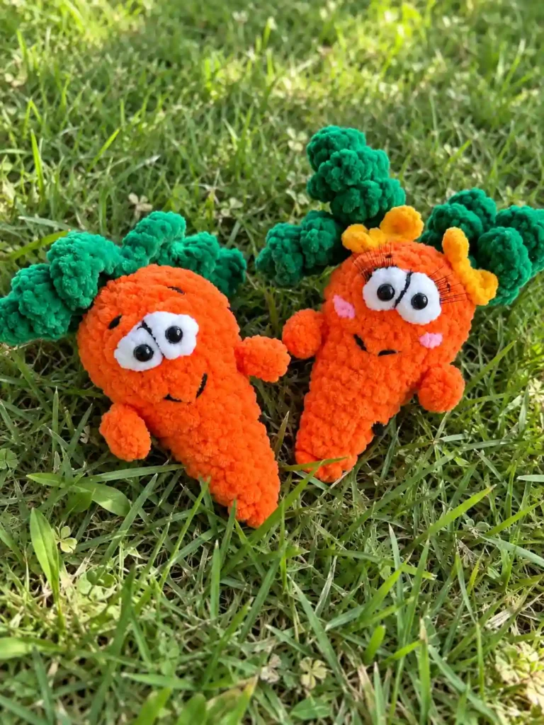 Two fuzzy orange carrot amigurumi pattern toys with curly green leaves sitting upright in a green grass lawn.
