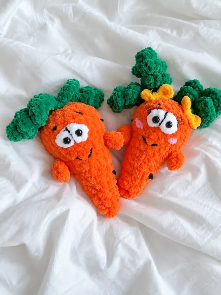 Two plush orange carrot amigurumi pattern dolls laid out together on a soft white crumpled bed sheet.