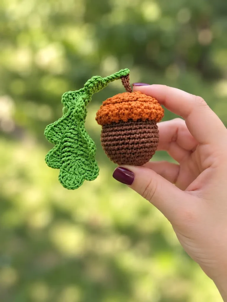 Hand holding a yarn toy from a crochet acorn pattern against a bright, blurred green outdoor nature background.