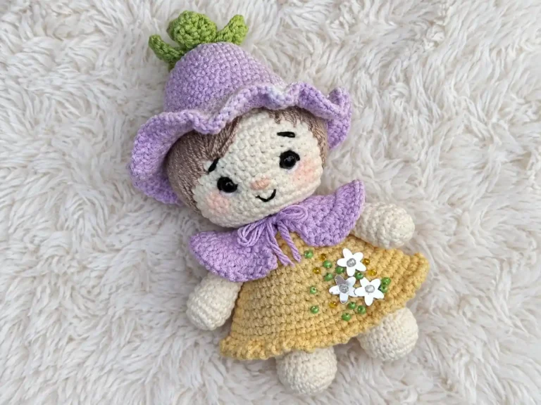 Hand holding a finished crochet gnome pattern doll with a purple hat and yellow dress against a blurred lake and trees.
