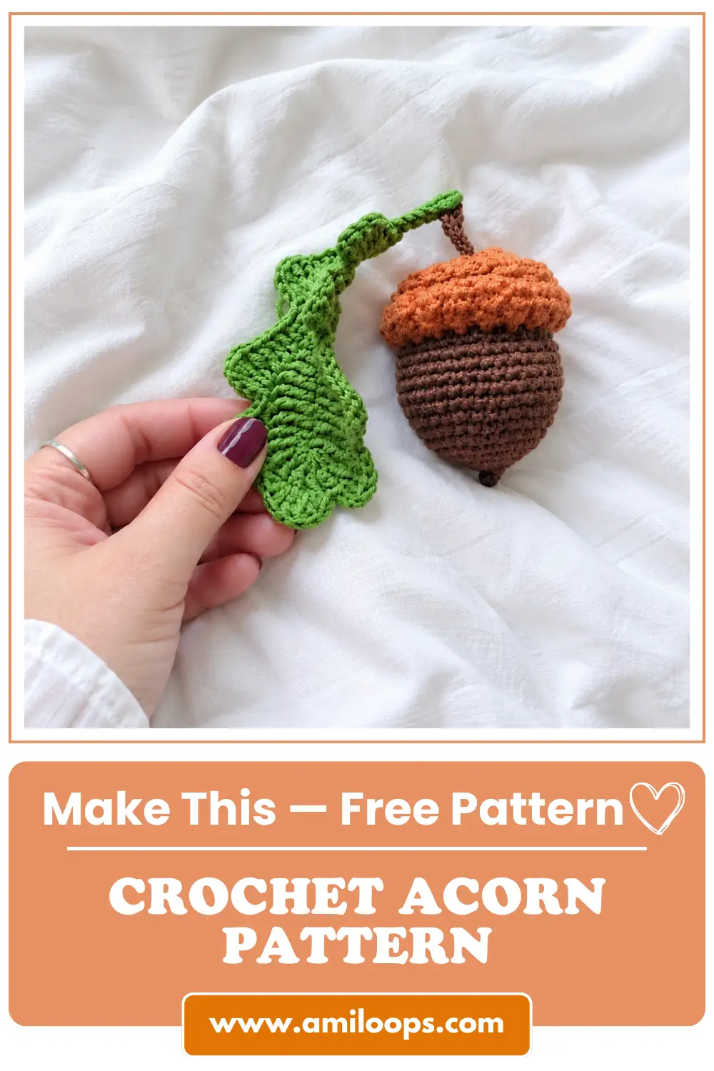 Hand holding a green crocheted leaf attached to a brown and orange toy from a crochet acorn pattern on white fabric.