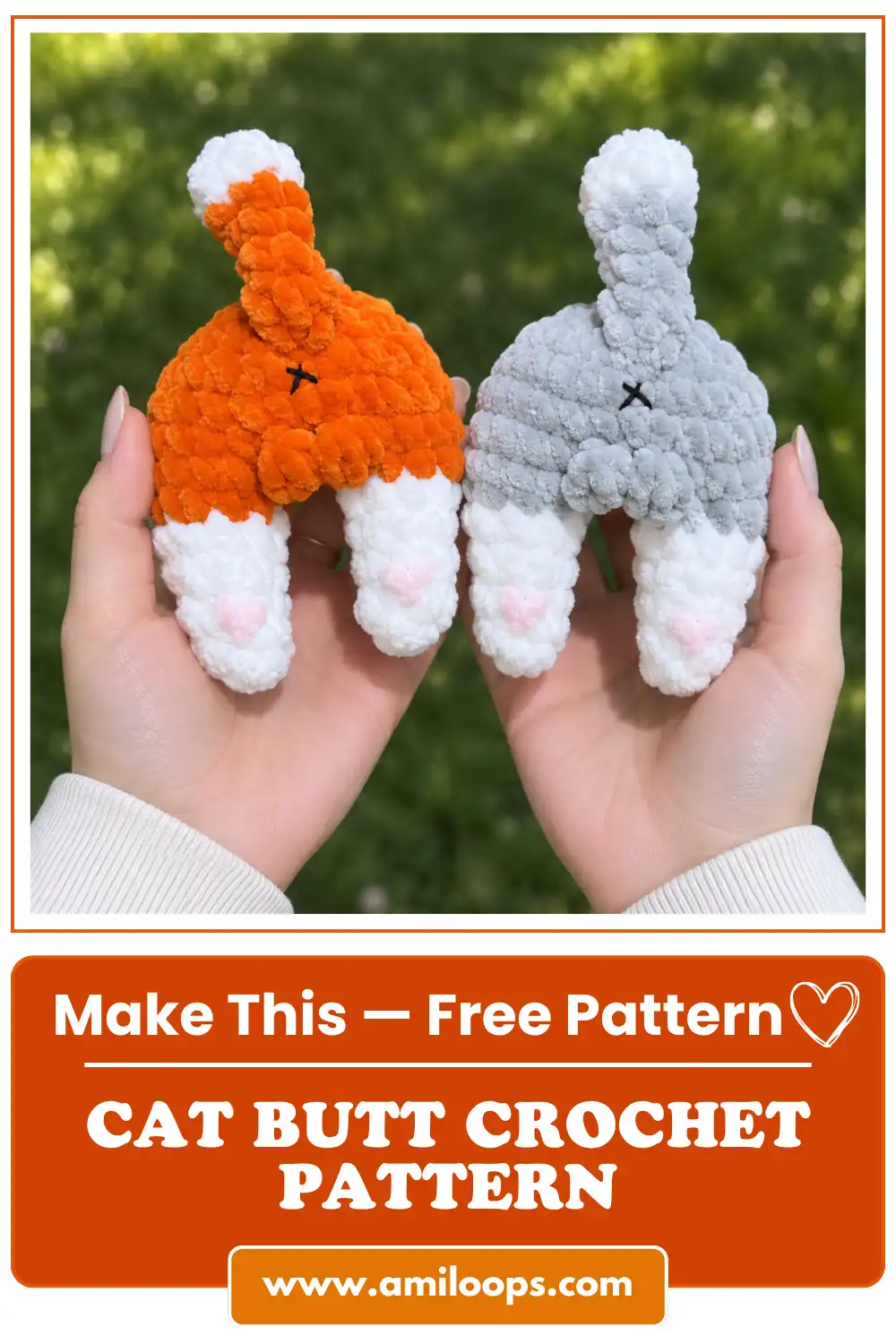Two hands holding orange and grey velvet yarn toys from a cat butt crochet pattern against a blurred green grass background.