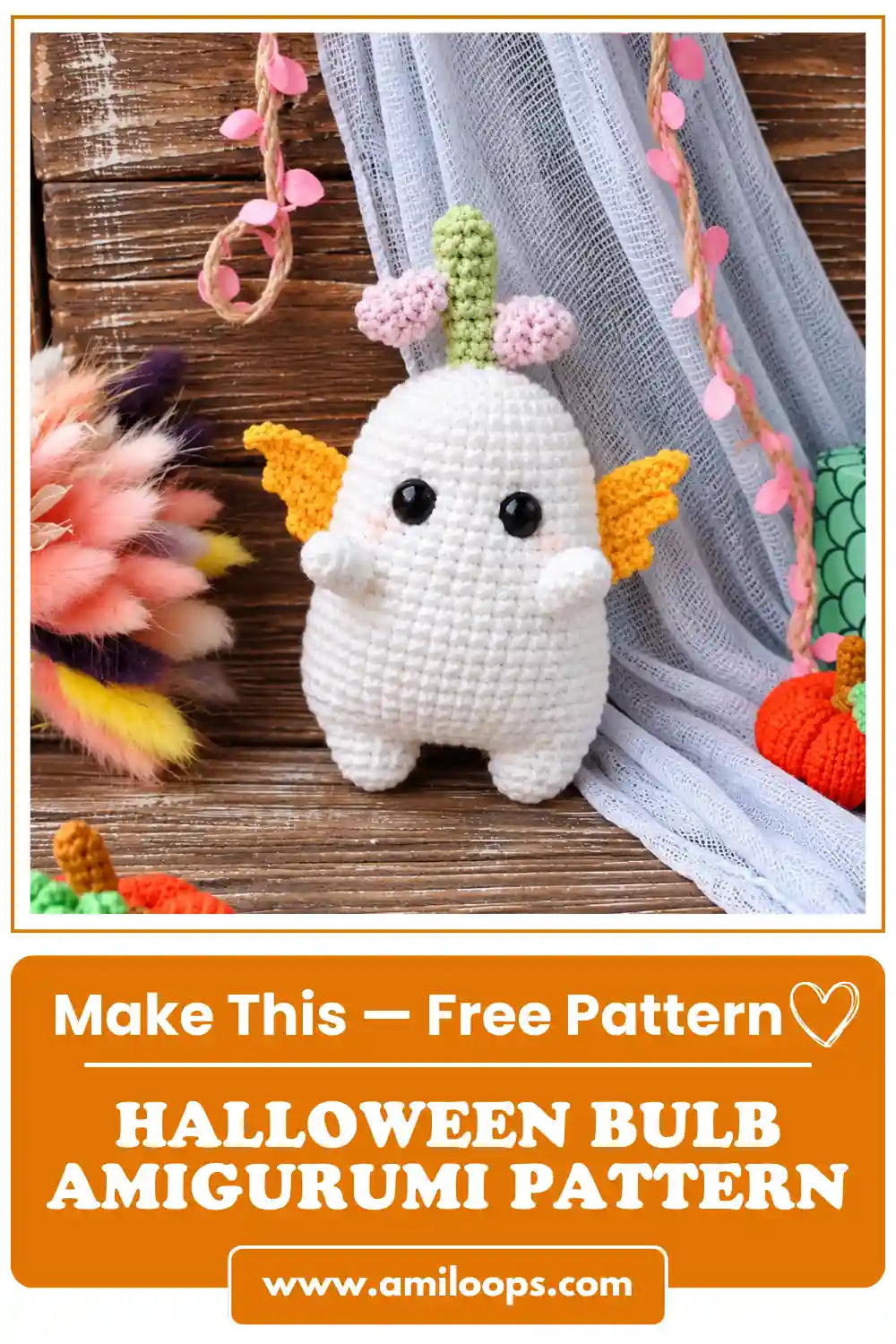 White bulb amigurumi pattern toy with yellow wings standing on wood with orange crochet pumpkins.