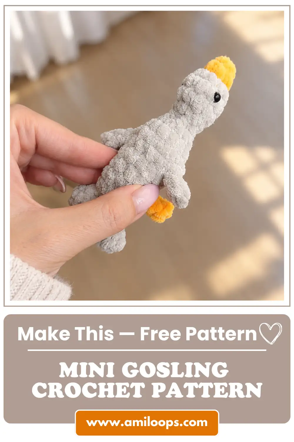 Vertical view of a hand holding a soft grey and yellow mini gosling crochet toy over a wooden floor