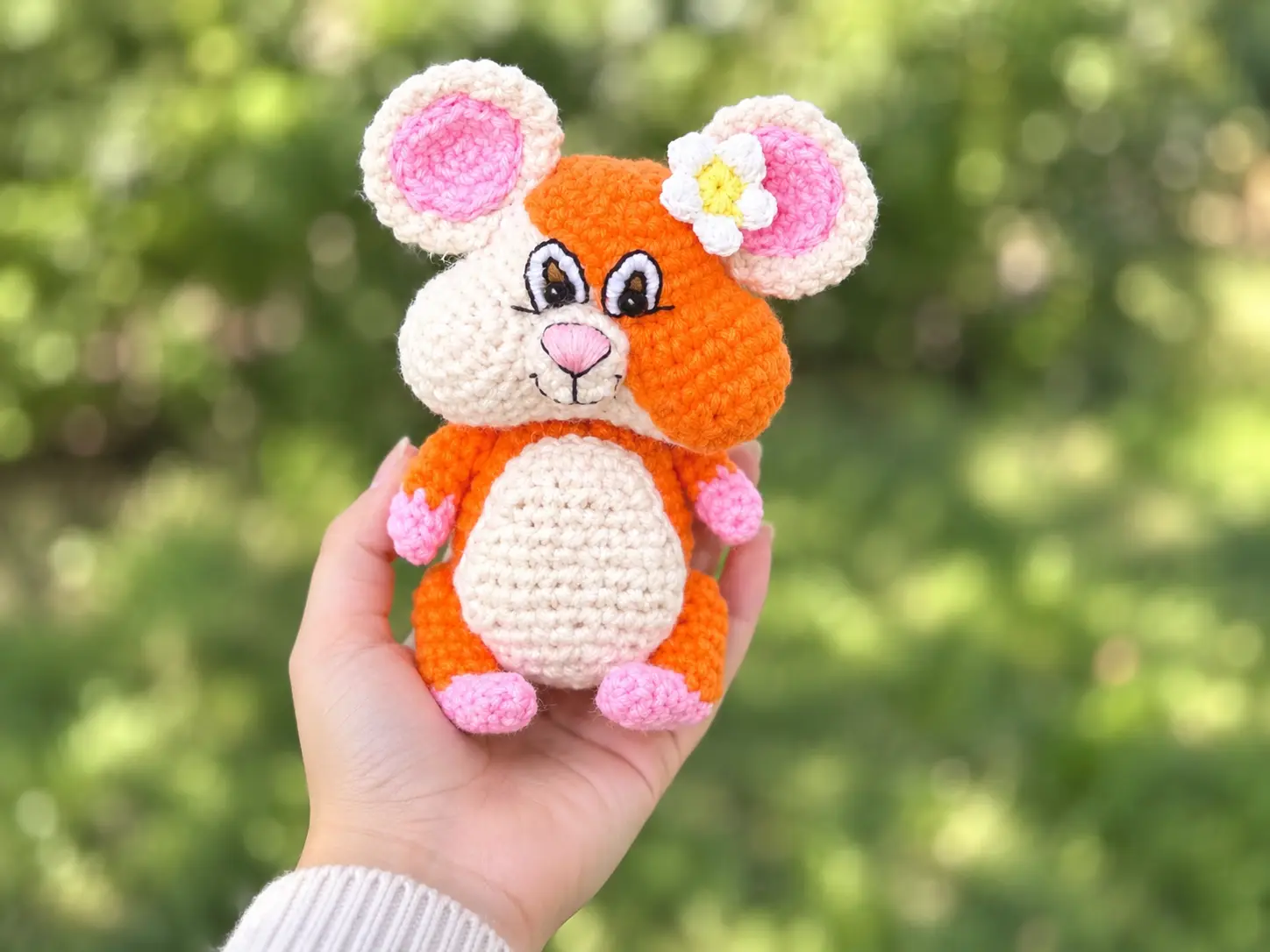 Hand holding a small orange crochet hamster outdoors, plus two photos of it sitting on a wooden table.