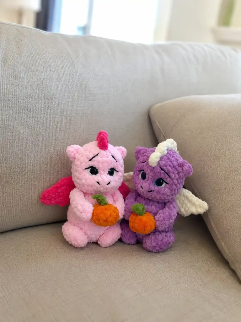 Plush pink and purple toys from a little dragon crochet pattern holding tangerines on a couch.