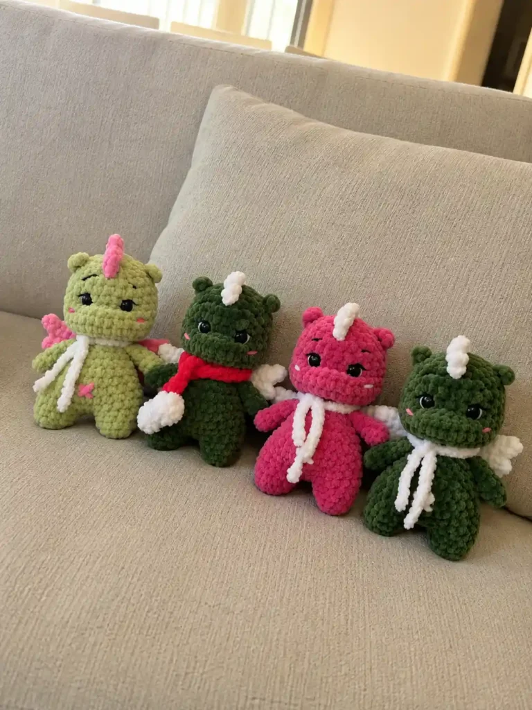 Four colorful plush dragons sitting in a row on a beige couch, displaying variations of the mini dragon amigurumi pattern.