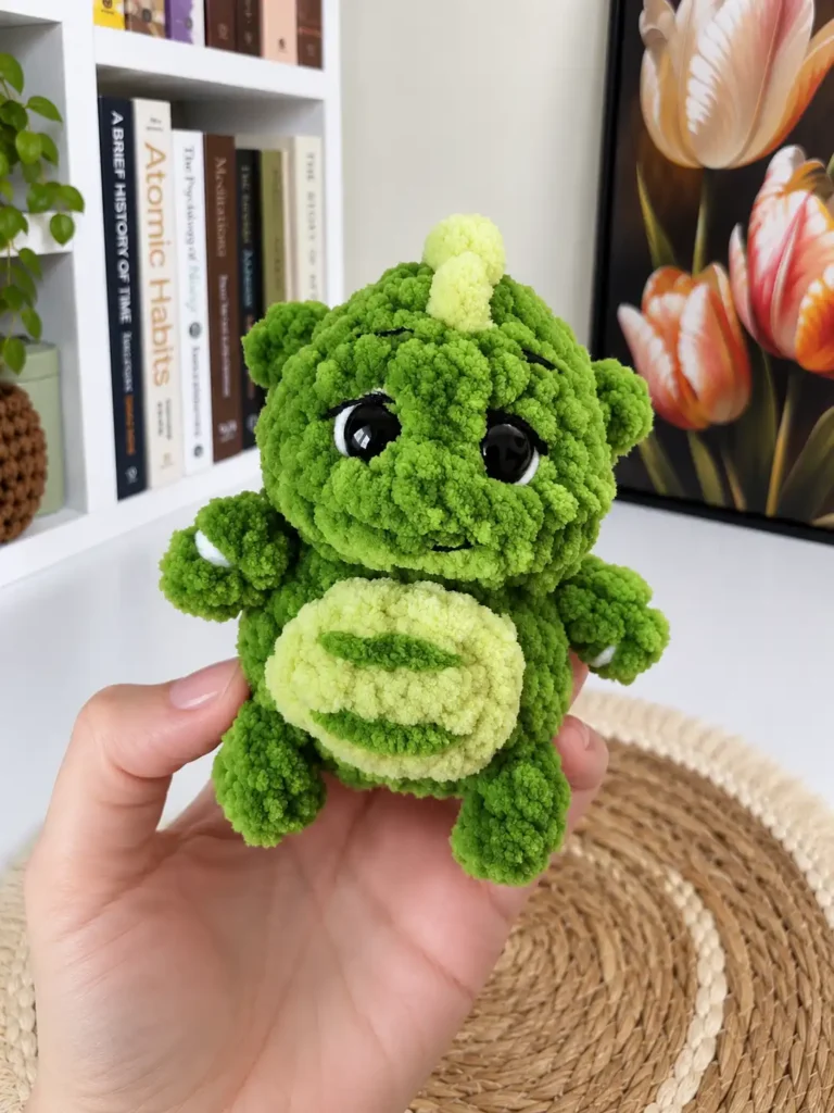 Hand supporting the green plush mini dragon crochet pattern from underneath to display the seamless joined legs.