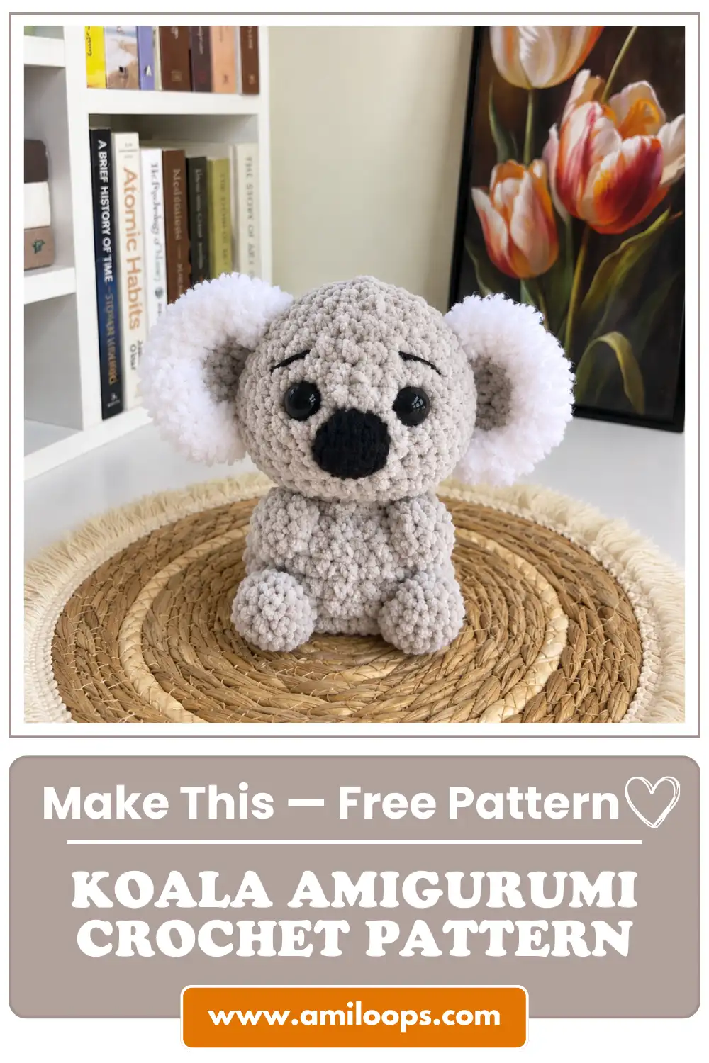 Plush grey koala amigurumi crochet pattern sitting on a woven mat near books and floral art.