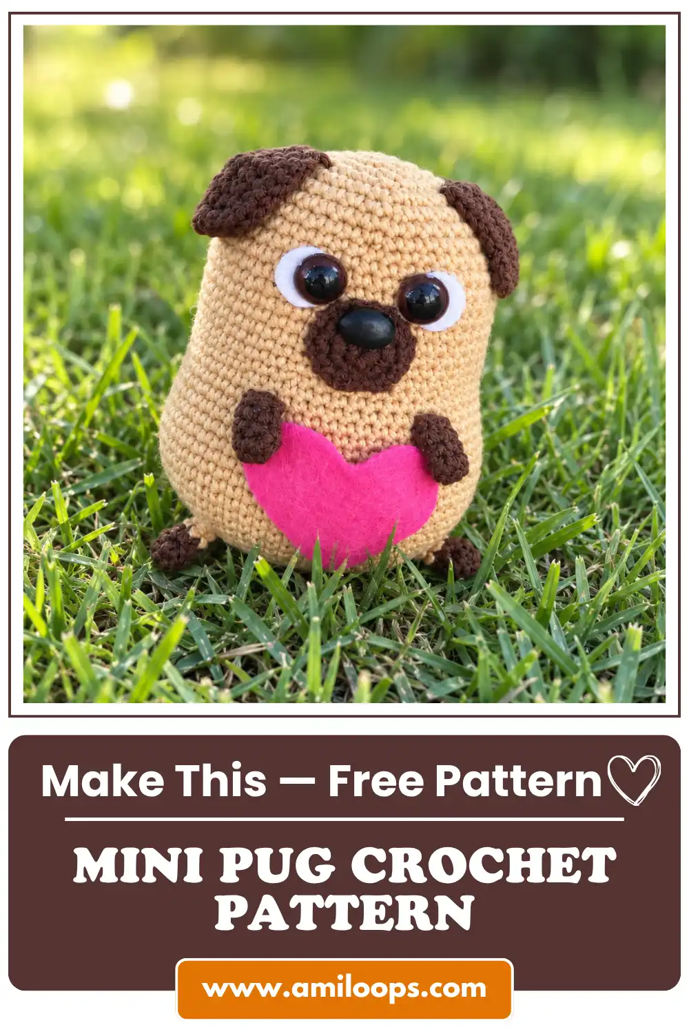 Amigurumi mini pug toy in beige yarn holding a pink felt heart sitting outdoors on green grass.
