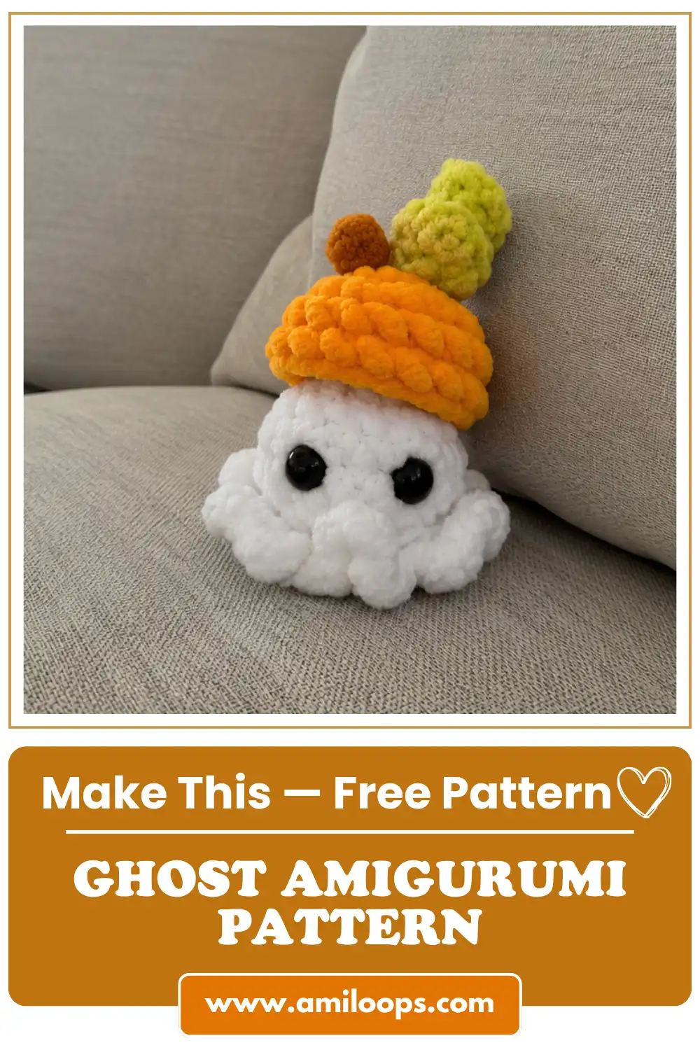 A white plush yarn toy made from a ghost amigurumi pattern, wearing an orange hat and sitting on a beige couch.