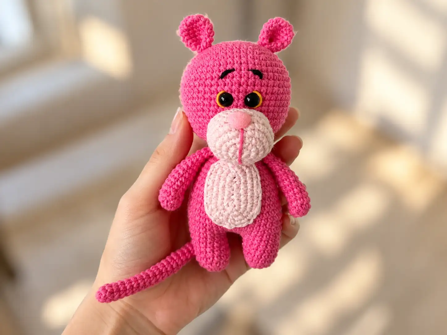 Pink and light pink crochet Pink Panther amigurumi shown held indoors, lying on a blanket, and held intdoors.