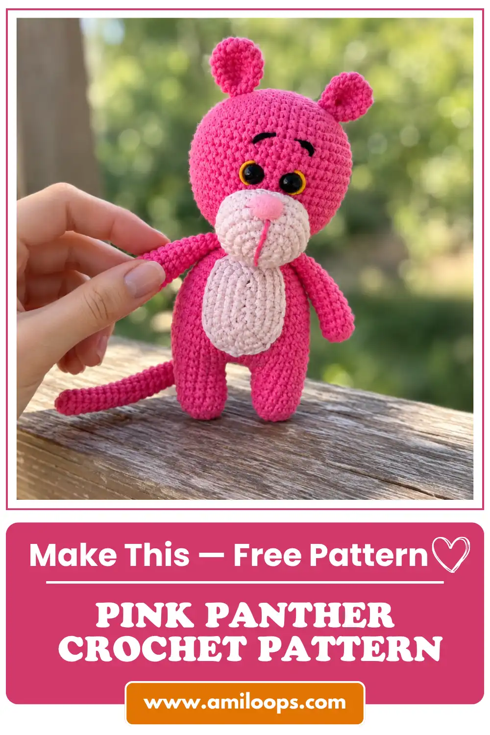 Finished bright pink yarn toy from a Pink Panther crochet pattern standing on an outdoor wooden railing, held by a hand.