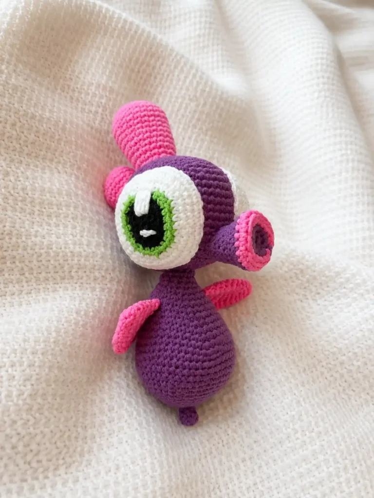 Purple and pink sea horse amigurumi pattern plush toy lying on a textured white knit blanket.