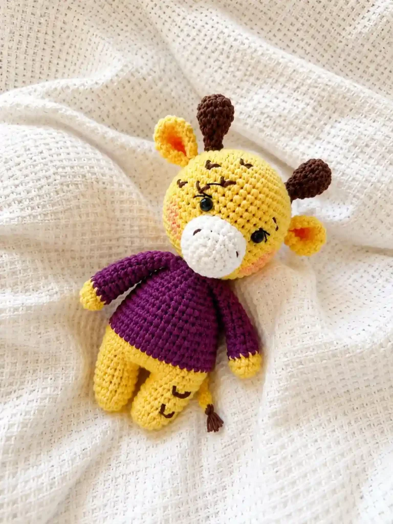 Yellow and purple amigurumi toy from our giraffe crochet pattern resting on a soft, textured white blanket.