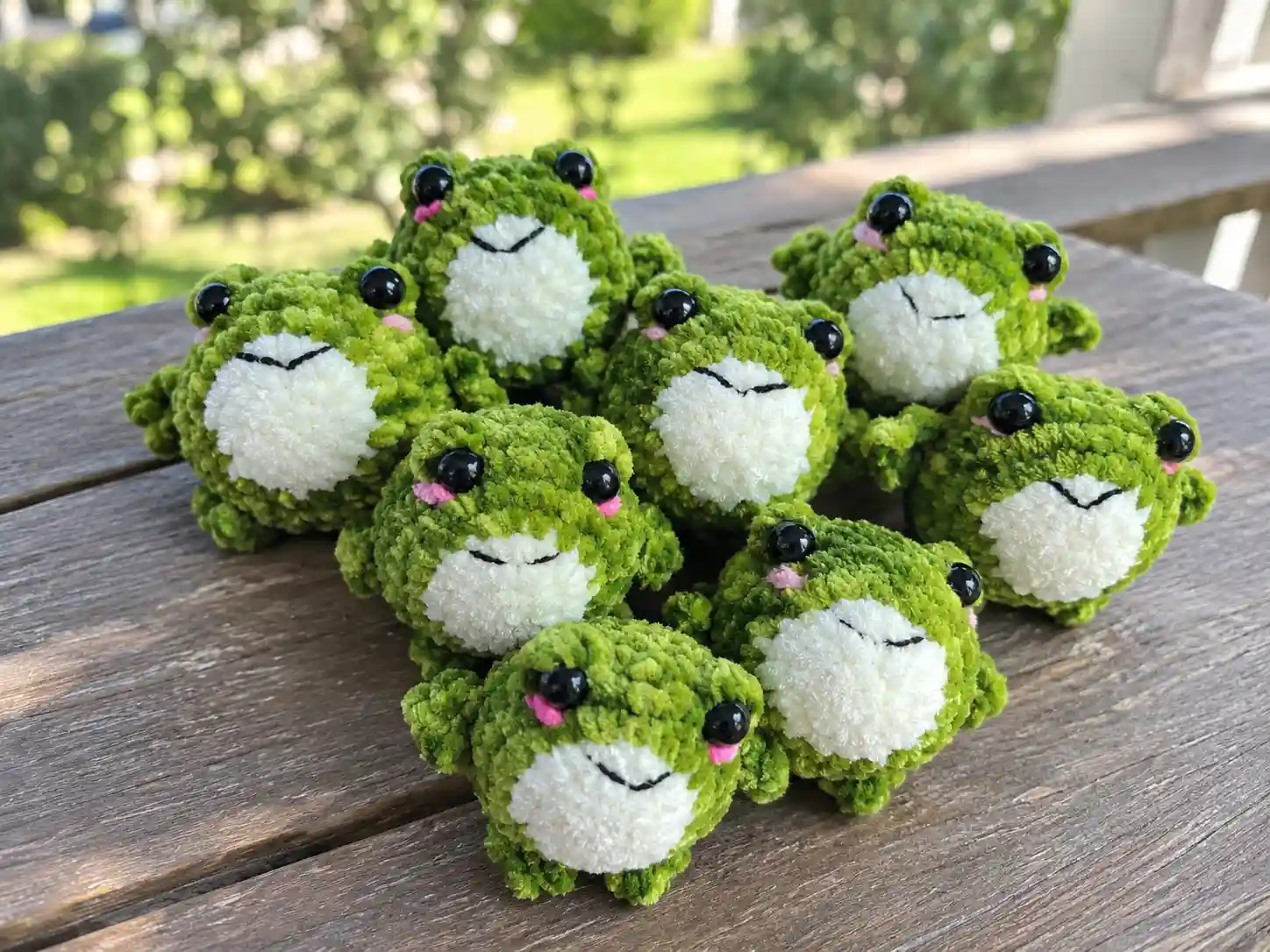 A group of green and white velour frog amigurumi toys with black eyes on a wooden table.