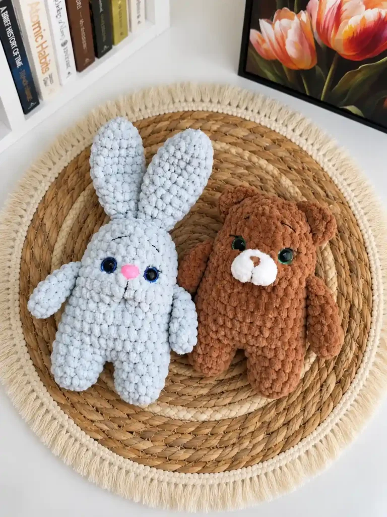Handmade light blue crochet bunny and brown crochet bear sitting side by side on a round woven straw mat.