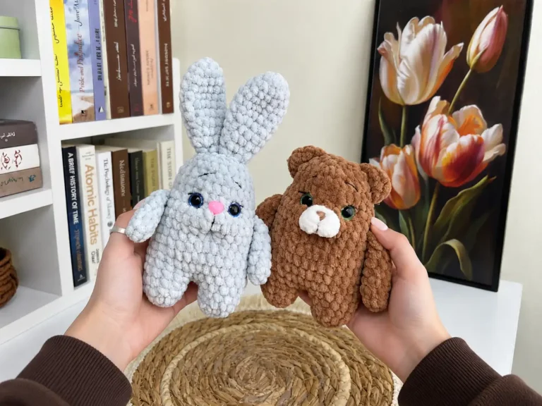 Hands holding light blue bunny and brown bear plush toys made with fluffy yarn, with a bookshelf and tulip painting background.