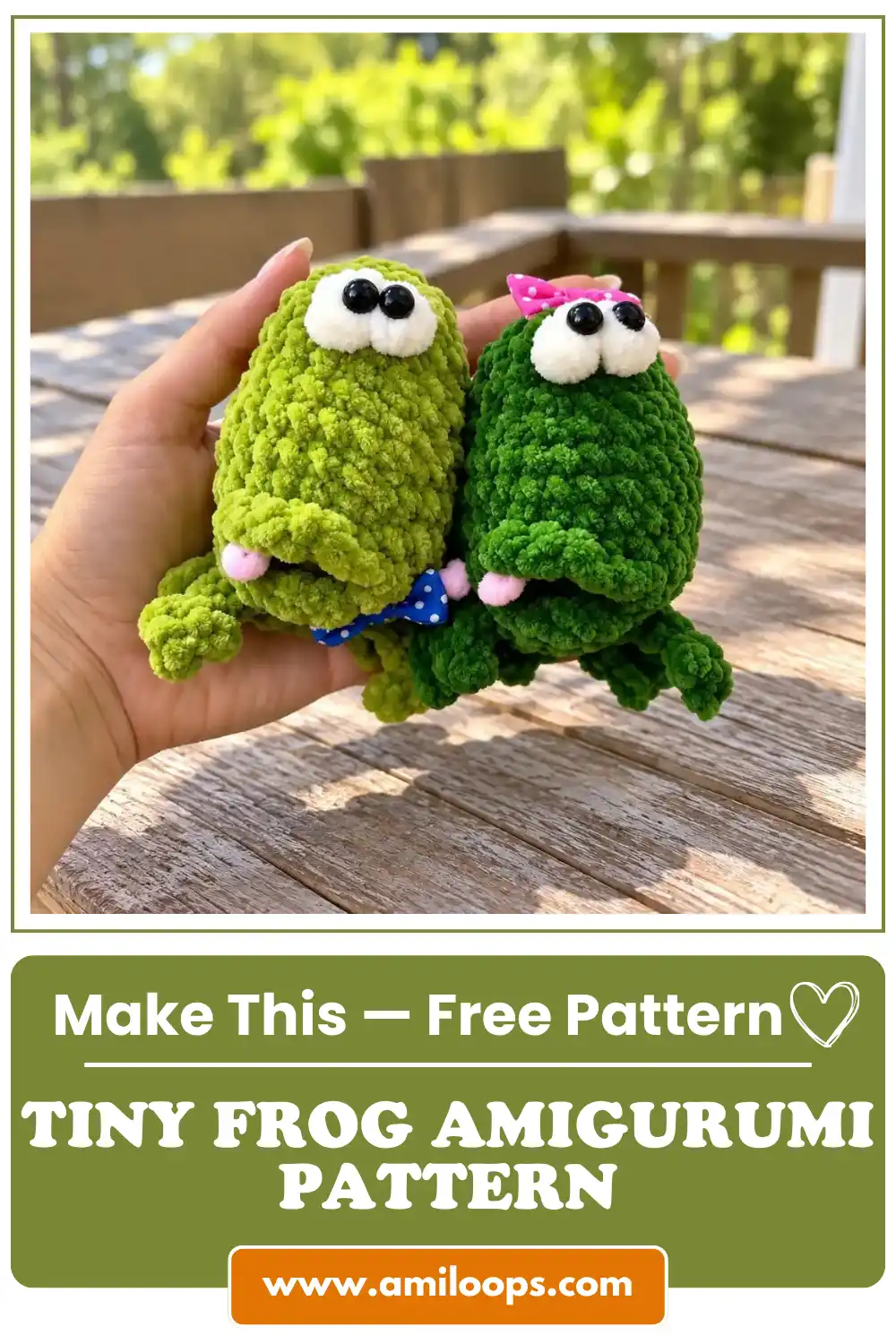 A hand holding two fuzzy green amigurumi crochet frogs with bows on a wooden deck in soft natural daylight.