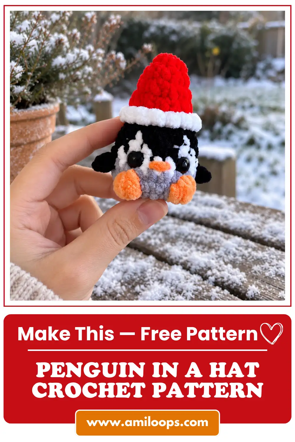 Hand holding a small black and white plush yarn penguin wearing a red Santa hat against a snowy garden backdrop