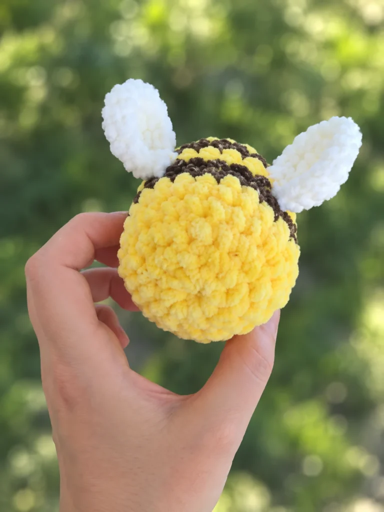 Back view of the plush bee amigurumi held in an open hand, highlighting the white wings and brown stripes.